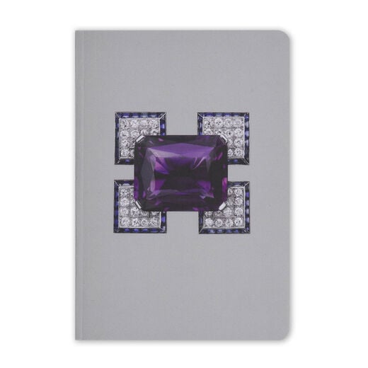 A grey pocket-sized notebook featuring an angular diamond brooch with a large purple amethyst at its centre