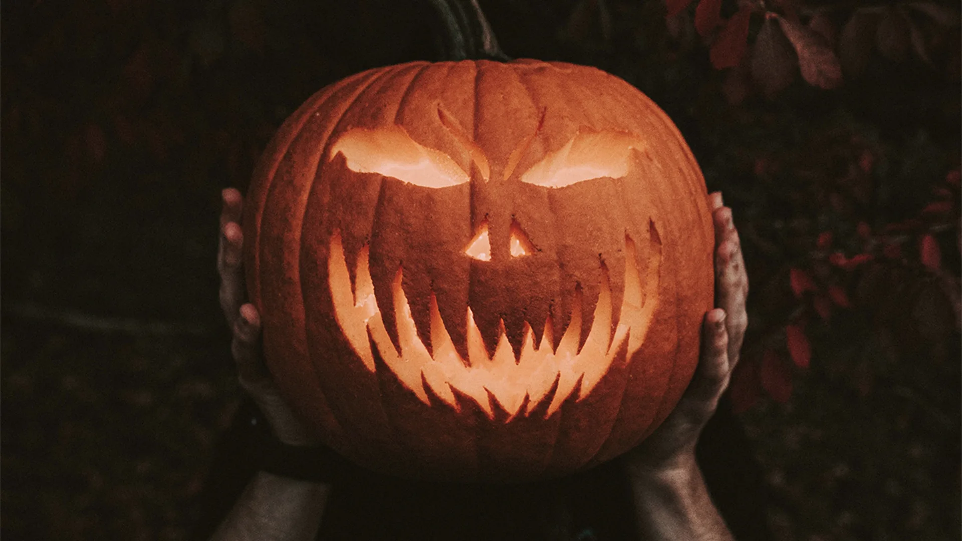 Someone's hands holding up a pumpkin with a scary face carved into it